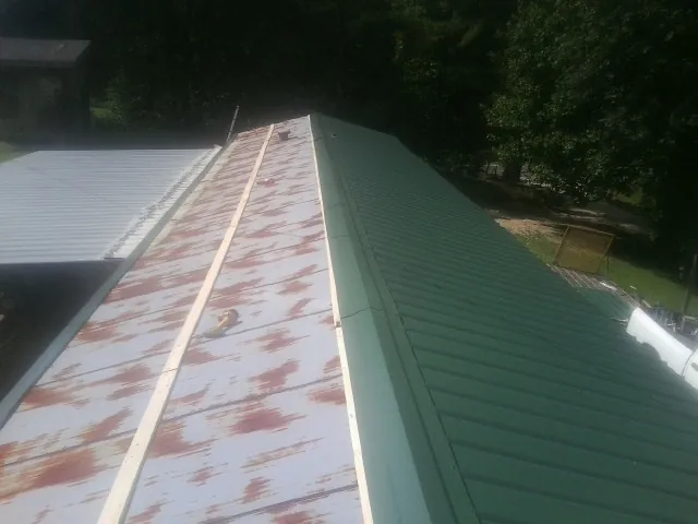 Old rusted panels beside newly installed green metal roofing — Wind Damage Roof Repair by Roofing Brothers in Church Hill